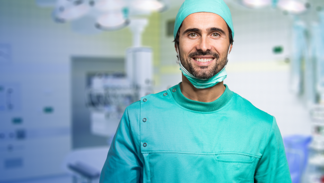 Bild eines lächelnden Chirurgen in einem grünen OP-Kittel in einem OP-Saal.
