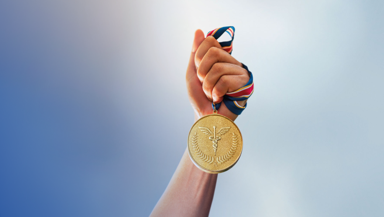  Imagen de una mano sujetando una medalla de oro en la que hay ramas de laurel y el caduceo.